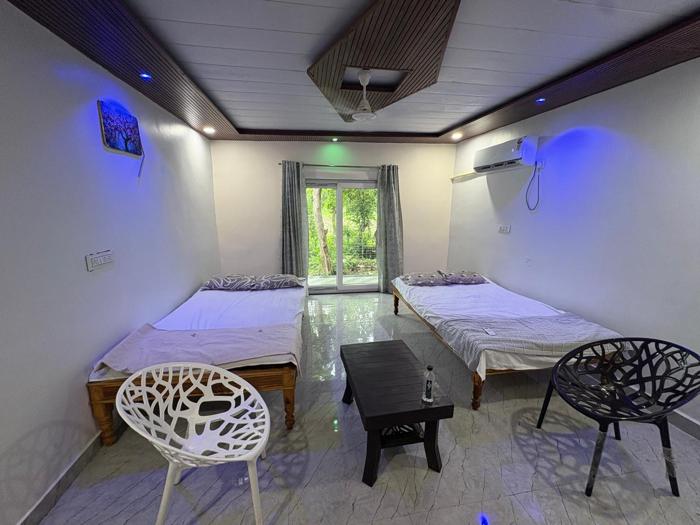 Room with two beds, two chairs and a sliding door looking onto greenery at the Nandai Gate stay.