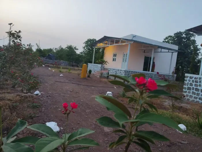 Cottage and covered veranda beyond flowering plants at Maya Stays – Bhavankhori · Kodori Gate.