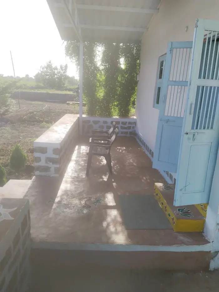 Chairs on the covered veranda beside pale blue doors at the Bhavankhori Gate stay.