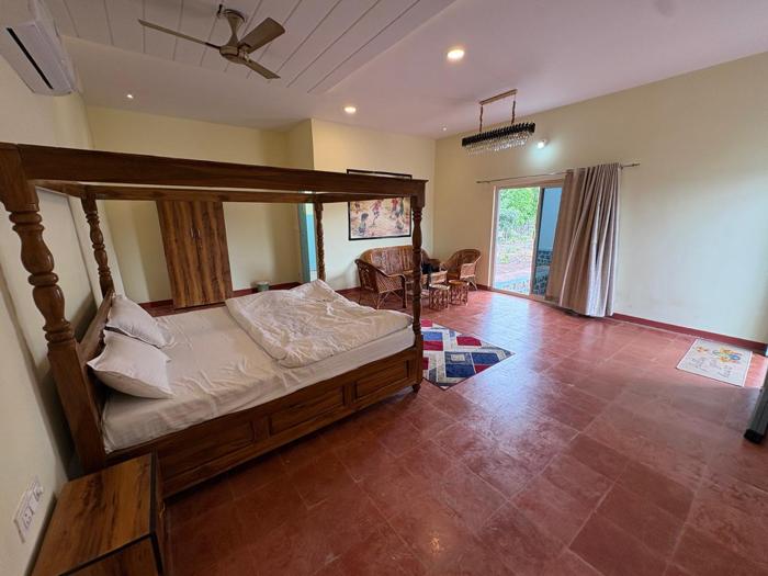 Four-poster bed and wicker chairs facing the glazed veranda door at the Bhavankhori Gate stay.